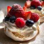 Mini pavlovas topped with whipped cream and fresh berries, light and airy.
